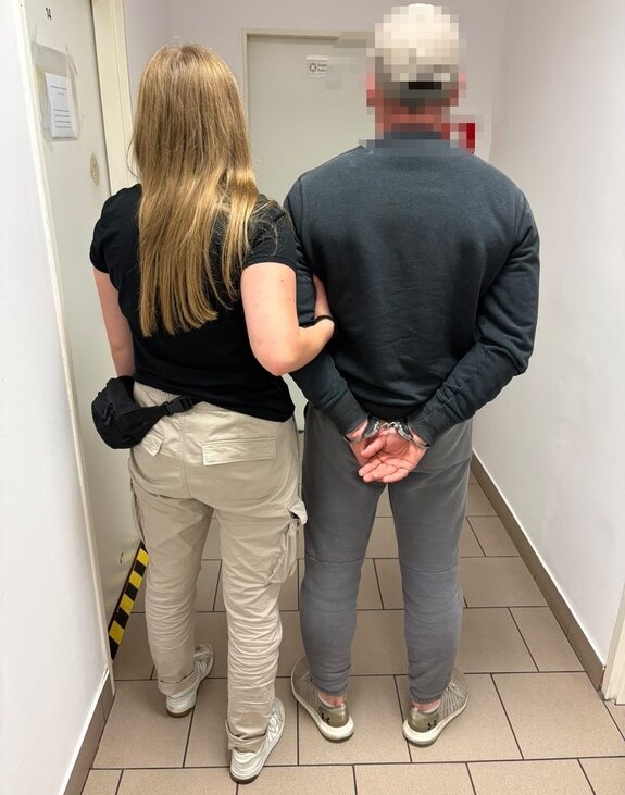 nieumundurowana policjantka prowadzi zatrzymanego skutego kajdankami przez korytarz jednostki