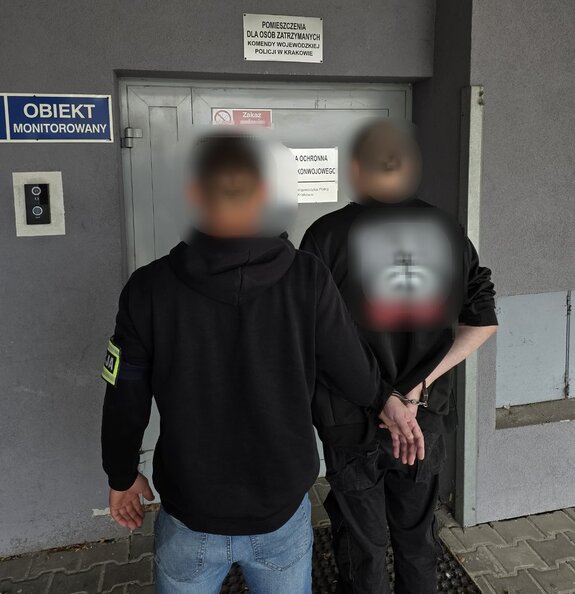 policjant bez munduru prowadzi zatrzymanego mężcyznę skutego kajdankami do pomieszczeń dla osób zatrzymanych