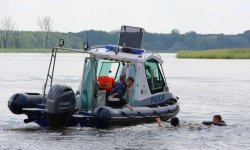 policyjna motorówka na jeziorze, na łodzi dwóch policjantów, obok dwie osoby w wodzie