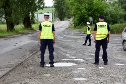 policjan t i strażnik ochrony kolei stojący tyłem, przed nimi idąca policjantka, w tle widać przejazd kolejowy