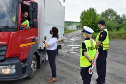 policjantka i pracownicy PKP rozmawiają i wręczają ulotki kierowcy tira ulotkę, w tle przejaz kolejowy