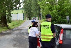 policjantka i pracownicy PKP wręczają kierowcy ulotkę, w tle przejaz kolejowy