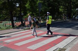 umundurowany policjant ruchu drogowego przeprowadzający dziecko przez jezdnię