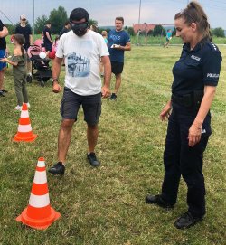 mężczyzna w alkogoglach przechodzący pomiędzy pachołkami, obok policjantka