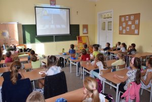 widoczne tyłem dzieci siedzące w klasie w ławkach podczas ogladania filmu edukacyjnego