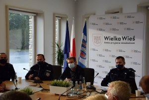 siedzący przy stole komendant komisariatu w Zielonkach obok wójt i z-ca naczelnika WRD KPP Kraków, obok dzielnicowy, za nimi baner gminy Wielka Wieś