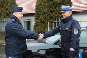 uścisk dłoni policjantów na tle nowego radiowozu.