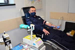 policjant podczas oddawania krwi, obok  waga z workiem napelnianym krwią
