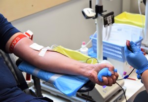 ręka z wbitą igłą podczas pobierania krwi i dłoń zaciskająca piłeczkę
