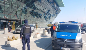 policjant patrolujący teren zewnetrzyny lotniska w Balicach, widoczny tylem do zdjęcia, obok zaparkowany radiowóz.