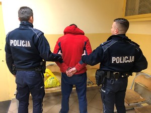 dwóch policjantów prowadzących zatrzymanego z kajdankami na ręce trzymane z tyłu