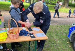 policjantka wykonująca daktyloskopie na policyjnym stoisku podczas pikniku rodzinnegom, w tle chodzące dzieci i dorośli