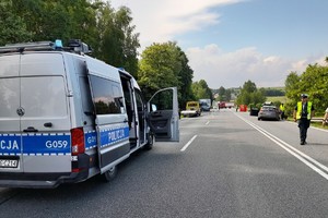 miejsce wypadku drogowego, widoczny radiowóz, w tle kolejny, chodzący policjanci ruchu drogowego, po prawej namiot za którymi leżą zwłoki