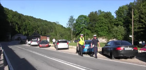 dwóch policjantów ruchu drogowego, jeden w kamizelce odblaskowej, idący wzdłóż drogi przy zaparkowamnych na poboczu pojazdach, w tle ojcowski park narodowy