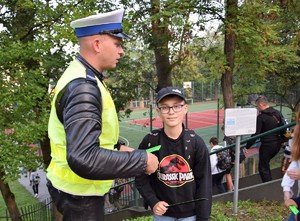 policjant stojący bokiem rozdający odblaski, obok niego uczeń z opaską odblaskową w ręce