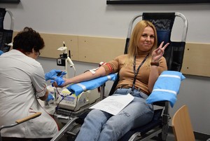 pracownik cywilny siedzący na fotelu podczas oddawania krwi, z podniesionymi dwoma palcami ku górze