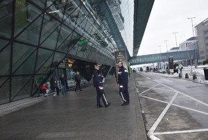 dwóch policjantów stojących przed budynkiem lotniska, w tle przechadzający się ludzie