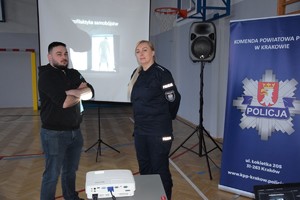 policjantka w mundurze obok policyjny psycholog, stoją przodem do zdjęcia, za nimi ekran z prezentacją, obok baner KPP Kraków (2)