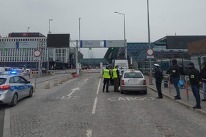 policjanci wspólnie z funkcjionariuszami  ITD i SG kontrolują pojazd - przewoźnika aplikacji mobilnej, po drugiej stronie widoczny radiowóz, w tle budynek lotniska