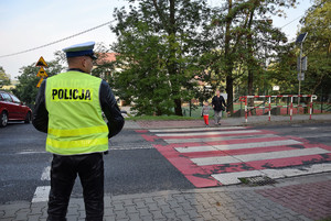 policjant stojący przed pasami w tle przechodząca przez pasy matka z dzieckiem