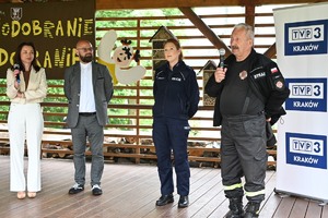 policjantka, obok niej mężczyzna z mikrofinem, z drugiej strony dwoje innych uczestników pikniku, obok baner TVP Kraków