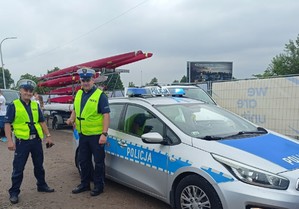 patrol ruchu drogowego stojący przy radiowozie, w tle kajaki ułozone na stojakach