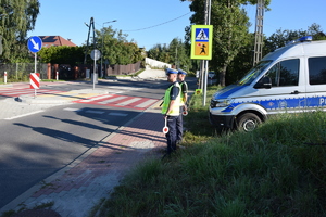 policjanci ruchu drogowego stojący przed przejściem dla pieszych, za nimi zaparkowany radiowóz