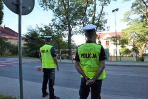 dwóch policjantów ruchu drogowego stojących przy drodze, w tle przed nimi szkoła