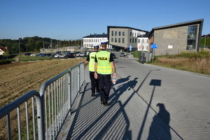 dwóch policjantów ruchu drogoqwego idących chodnikiem w stronę szkoły