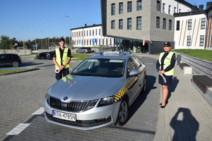 funkcjonariuszka straży gminnej i policjant stojący przy pojeździe straży gminnej, w tle szkoła