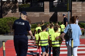 dwoje policjantów przeprowadza dzieci ubrane w kamizelki odblaskowe przez jezdnię