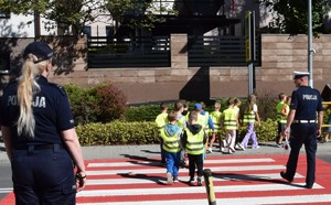 dwoje policjantów przeprowadza przez jezdnię dzieci ubran e w kamizelki odblaskowe z napisem bezpieczny powiat krakowski