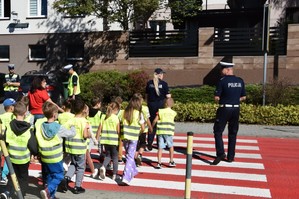 dwoje policjantów przeprowadza dzieci ubrane w kamizelki odblaskowe przez jezdnię. (2)