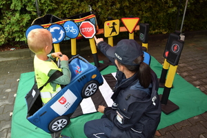 dziecko z policjantką przy stoisku policyjnym z zabawkowymi znakami drogowymi