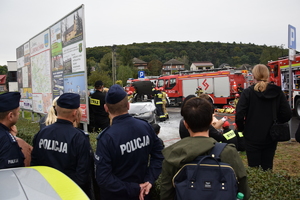 policjanci i inne osoby obserwujące pokaz straży pożarnej - spalonego samochodu i ewakuacji osób