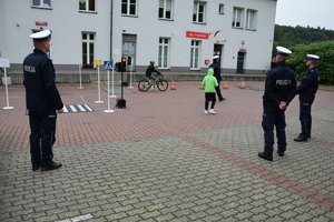chłopak na rowerze zdający egzamin praktyczny na kartę rowerową, przy miasteczku rowerowym stojących czterech policjantów