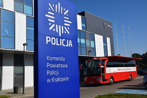 banek Komendy Powiatowej Policji w Krakowie, w tle zaparkowany krwiobus przed komendą