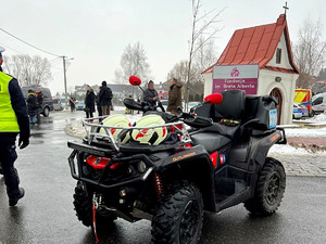 qud, obok idący policjant, w tle ludzie i zaparkowany radiowóz oraz kapliczka (2)